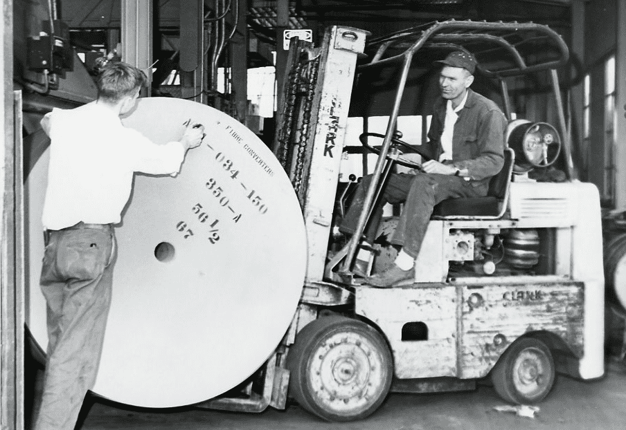 A worker marking a roll of paper while a forklift operator waits, at the original Three Rivers plant around 1950